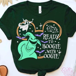 May include: A dark green short-sleeve t-shirt featuring a graphic of a light green stitched character, a white ghost dog, dice, and purple bats. The design includes the text READY TO BOOGIE WITH OOGIE in white, framed by an orange Mickey Mouse ear outline.
