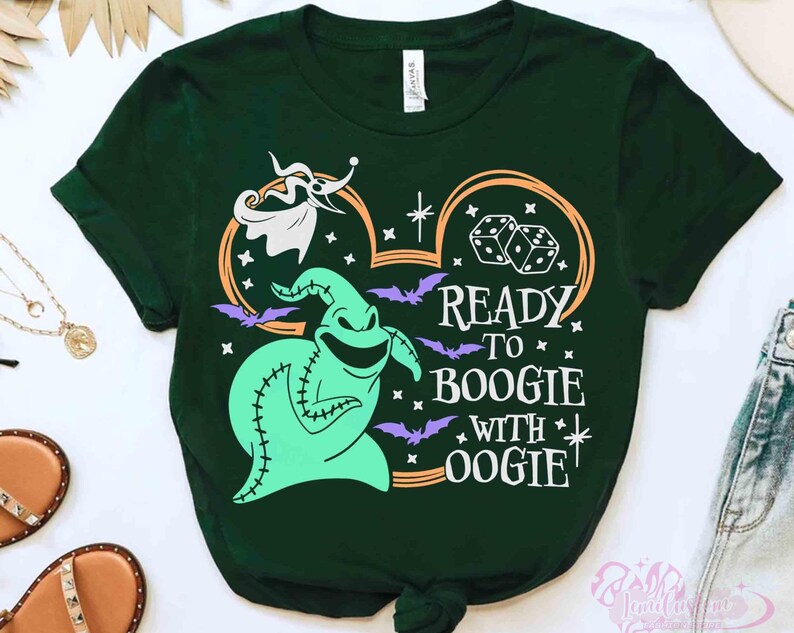 May include: A dark green short-sleeve t-shirt featuring a graphic of a light green stitched character, a white ghost dog, dice, and purple bats. The design includes the text READY TO BOOGIE WITH OOGIE in white, framed by an orange Mickey Mouse ear outline.