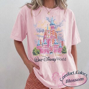 Op de afbeelding: Lichtroze T-shirt met een afbeelding van het kasteel van Assepoester en de tekst "This is Now! Walt Disney World 1997". Het shirt is van Comfort Colors Blossom.
