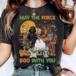 May include: Dark gray t-shirt with a Halloween-themed graphic. The design features Star Wars characters as skeletons and ghosts, with the text "MAY THE FORCE BOO WITH YOU" in green. A full moon and bats are in the background.