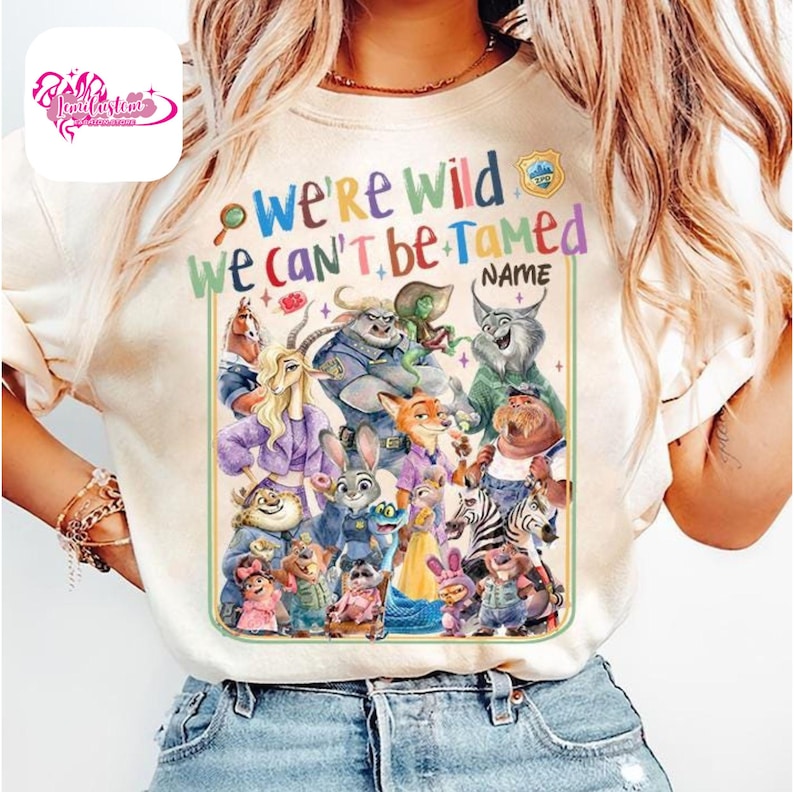 Puede incluir: Camiseta color crema con un gr&aacute;fico colorido de personajes de Zootopia. El texto "We're Wild, We Can't Be Tamed" est&aacute; encima de los personajes. Una peque&ntilde;a insignia est&aacute; en la esquina superior derecha. La camiseta es de cuello redondo.