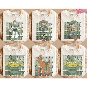 May include: Six off-white t-shirts featuring various Toy Story character graphics. Each shirt has a different character design, including Buzz Lightyear, Jessie, Woody, and others, with the text "Howdy" in green.