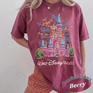 Op de afbeelding: Bessenkleurig T-shirt met een afbeelding van het kasteel van Assepoester en de tekst "This is Now! Walt Disney World 1971". Het shirt is van het merk Comfort Colors.