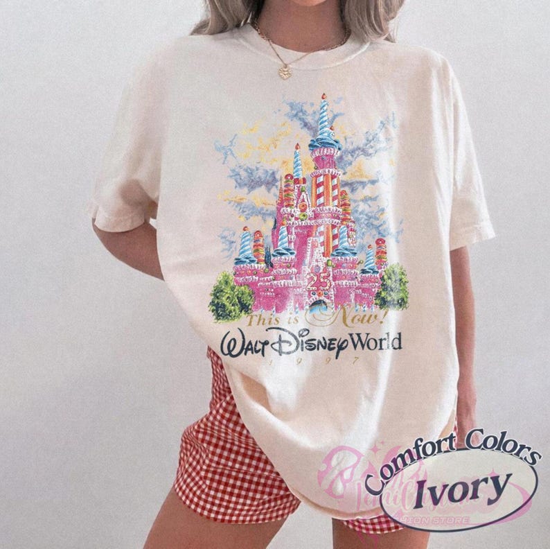 Op de afbeelding: Ivoor T-shirt met een kleurrijke illustratie van een kasteel en de tekst "This is Now! Walt Disney World 1997". Het shirt heeft een klassieke pasvorm en korte mouwen. Het shirt is gemaakt van een zacht materiaal.