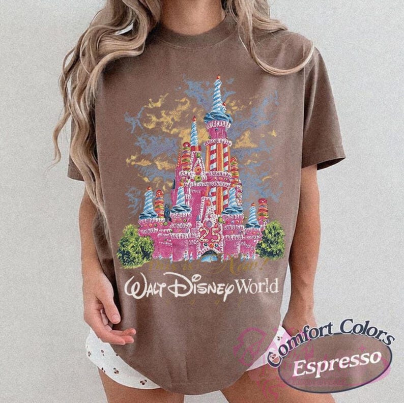 Op de afbeelding: Bruin t-shirt met een roze kasteelontwerp, blauwe en gele accenten, het nummer 25 en de woorden "Walt Disney World". Het shirt heeft ook de woorden "Comfort Colors Espresso" erop gedrukt.