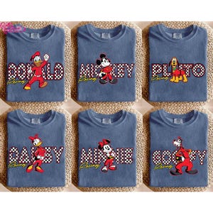 May include: Six blue t-shirts featuring Disney characters: Donald Duck, Mickey Mouse, Pluto, Daisy Duck, Minnie Mouse, and Goofy. Each shirt has the character's name in a checkered pattern and the word "Racing" in yellow.