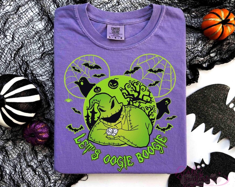 May include: A purple t-shirt with a green Oogie Boogie design, bats, ghosts, and the text "Let's Oogie Boogie." The design includes a green moon and spiderwebs. Halloween decorations surround the shirt.