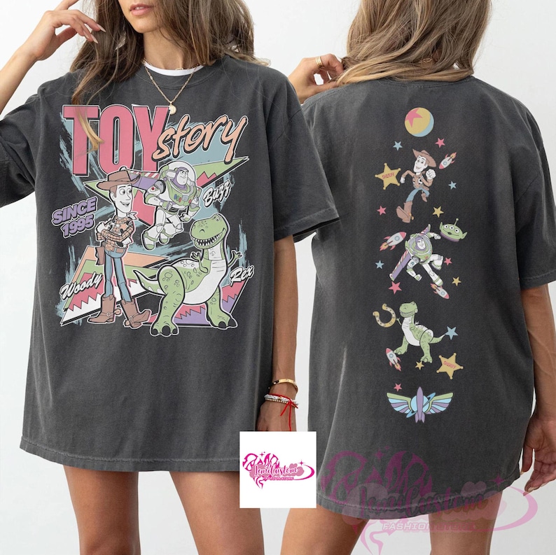 May include: Dark gray t-shirt featuring a Toy Story graphic. The front displays Woody, Buzz Lightyear, and Rex with the text "TOY STORY SINCE 1995". The back showcases various characters and elements from the movie. A casual, oversized tee.