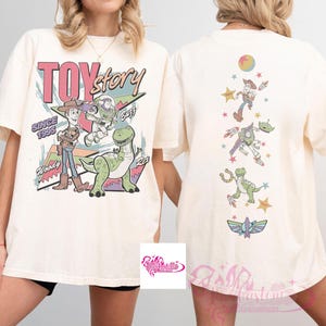 May include: Cream-colored t-shirt featuring a Toy Story graphic. The front displays Woody, Buzz Lightyear, and Rex with the text "TOY STORY SINCE 1995". The back showcases various characters. A fun, nostalgic design.