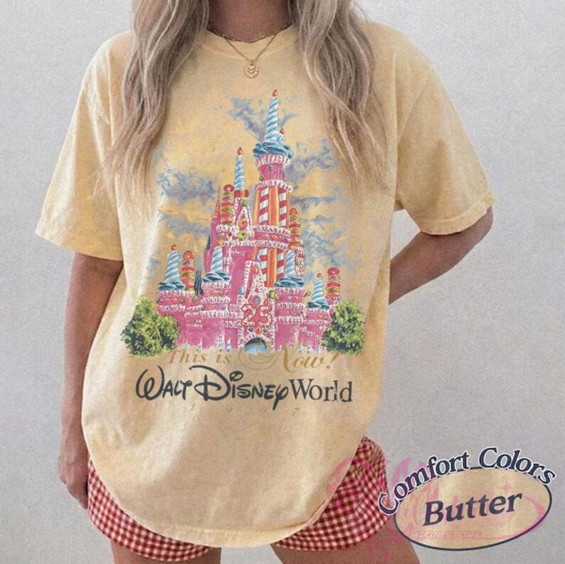 Op de afbeelding: Boterkleurig T-shirt met een kleurrijke illustratie van een kasteel met de tekst "This is Now! Walt Disney World". Het shirt heeft korte mouwen en een relaxte pasvorm. De tekst "Comfort Colors Butter" staat er ook op.