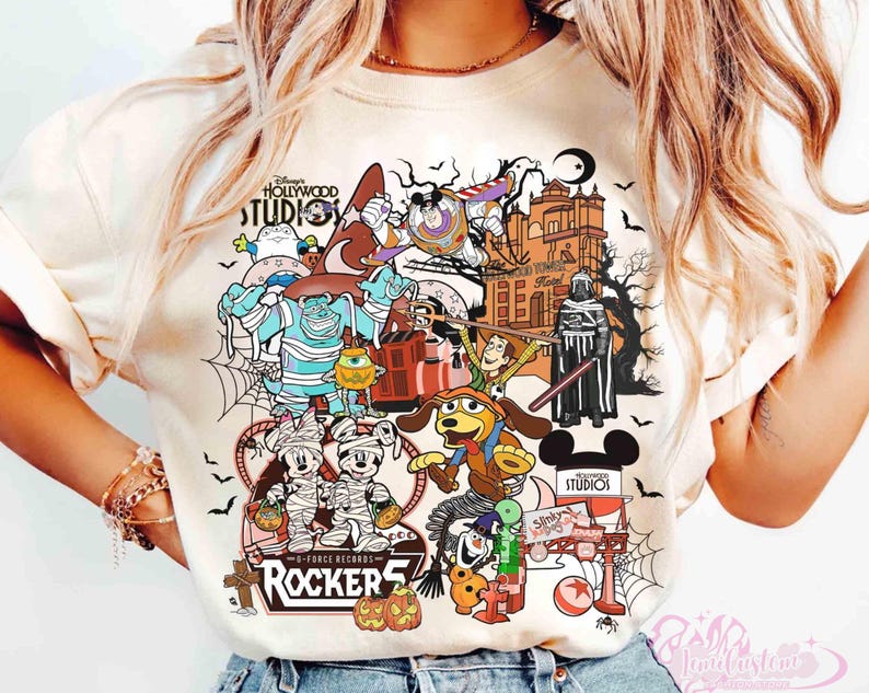 May include: A cream-colored t-shirt featuring a graphic print of various cartoon characters in Halloween costumes, including mummies, a space ranger, and a cowboy. The design includes the text Disney's Hollywood Studios, Rocker 5, and Slinky Dog.