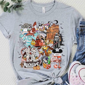May include: A heather gray short-sleeve t-shirt featuring a colorful graphic print of various Disney characters in Halloween costumes, including Mickey Mouse, Buzz Lightyear, and Sulley, with the text Disney Hollywood Studios and Rockers.