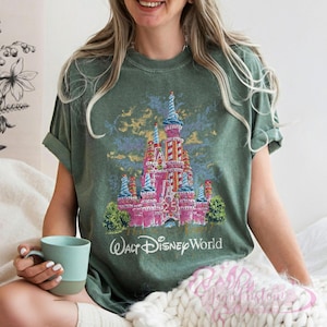 Op de afbeelding: Groen t-shirt met een roze kasteelafbeelding, blauwe en rode accenten, het nummer 25 en de tekst "Walt Disney World". De mouwen zijn opgerold.