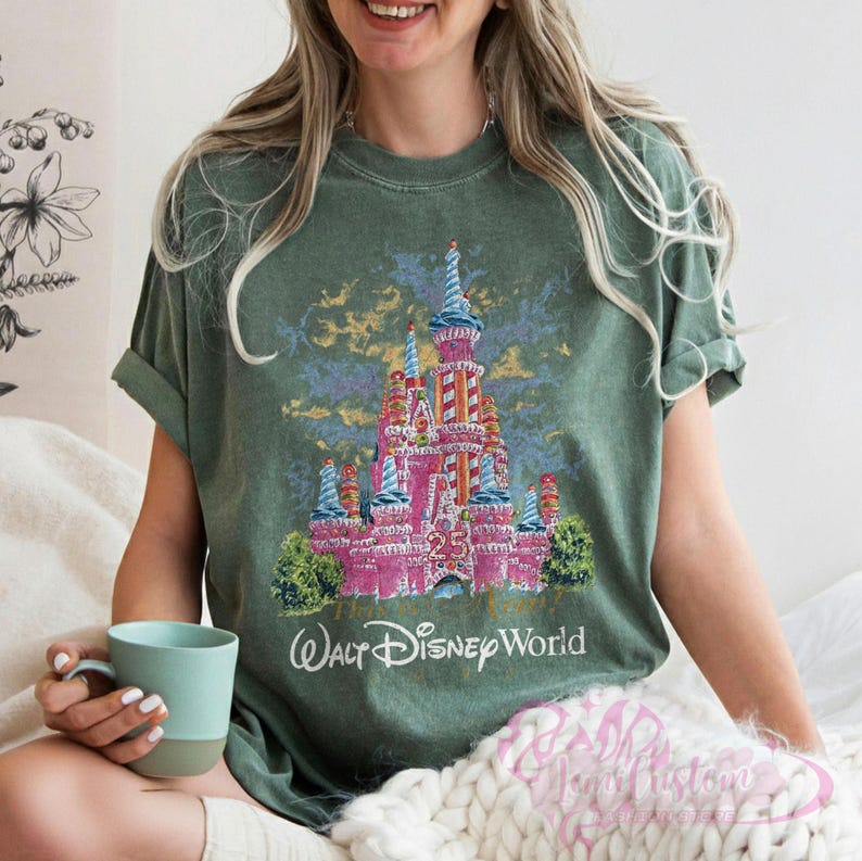 Op de afbeelding: Groen t-shirt met een roze kasteelafbeelding, blauwe en rode accenten, het nummer 25 en de tekst "Walt Disney World". De mouwen zijn opgerold.