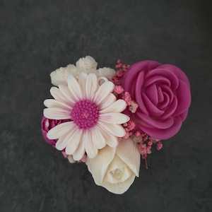 Peut inclure: Un arrangement floral décoratif composé d'une grande rose magenta, d'une marguerite blanche au centre magenta et d'un bouton de rose blanc plus petit. Les fleurs sont agrémentées de petites grappes de fleurs séchées roses et blanches.