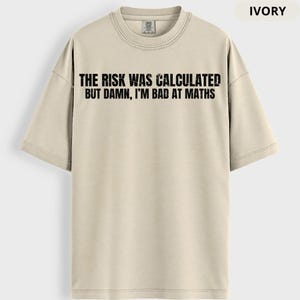 Peut inclure: T-shirt ivoire avec l'inscription noire "THE RISK WAS CALCULATED BUT DAMN, I'M BAD AT MATHS". Le t-shirt a un col rond et des manches courtes. Le t-shirt est de couleur neutre.