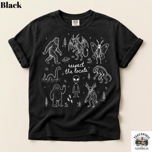 May include: A black short-sleeve t-shirt featuring a white graphic print of various cryptids and extraterrestrial figures, including Bigfoot, an alien, and a mothman. The text "respect the locals" is centered among the illustrations.