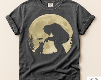May include: Pepper-colored t-shirt featuring a Bigfoot silhouette booping a cat's nose in front of a full moon. The word "BOOP" is above the cat. The shirt has rolled-up sleeves and a Comfort Colors tag.
