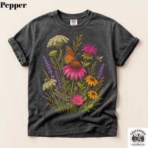 May include: A charcoal gray short-sleeve t-shirt featuring a vibrant botanical illustration of wildflowers, a monarch butterfly, a dragonfly, and a bee. The graphic includes pink coneflowers, purple lavender, and yellow daisies on the front.