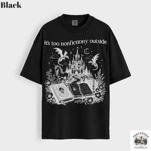May include: Black t-shirt with a fantasy-themed graphic. The design features a castle, dragons, a unicorn, and open books, with the text "it's too nonfictiony outside". The shirt has short sleeves and a crew neck.