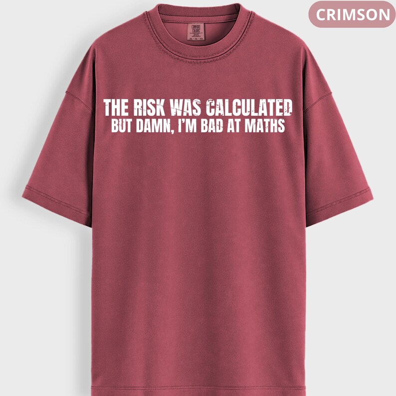 Peut inclure: T-shirt de couleur cramoisie avec l'inscription blanche : "THE RISK WAS CALCULATED BUT DAMN, I'M BAD AT MATHS". Le t-shirt a un col rond et des manches courtes. Le mot "CRIMSON" est dans un encadr&eacute; en haut &agrave; droite.