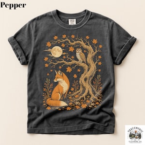 May include: A charcoal gray short-sleeve t-shirt featuring a graphic print of a fox sitting beneath a tree with an owl perched on a branch. The scene includes a full moon and orange autumn leaves. The shirt has a crew neck and rolled sleeves.