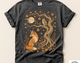 May include: A charcoal gray short-sleeve t-shirt featuring a graphic print of a fox sitting beneath a tree with an owl perched on a branch. The scene includes a full moon and orange autumn leaves. The shirt has a crew neck and rolled sleeves.