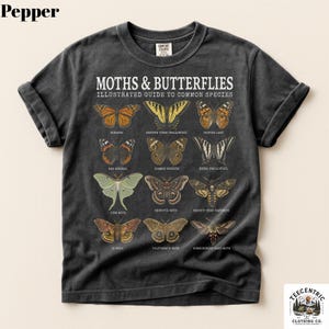 May include: A charcoal gray short-sleeve t-shirt featuring a graphic print titled MOTHS & BUTTERFLIES ILLUSTRATED GUIDE TO COMMON SPECIES. The design displays twelve detailed illustrations of various moth and butterfly species with their names printed below each.