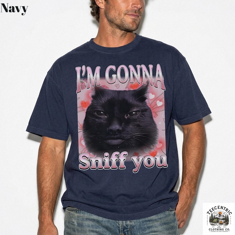 May include: Navy blue t-shirt with a black cat graphic and the text "I'M GONNA Sniff you" in pink and white. The design includes pink hearts. The shirt is from Teecentric Clothing Co.