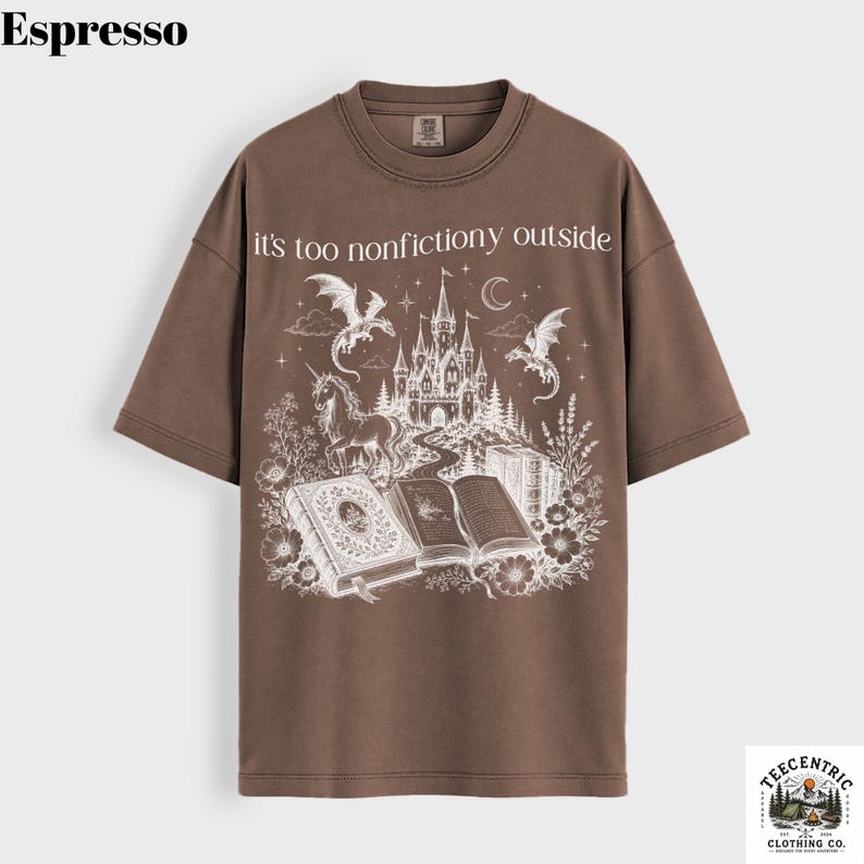 May include: Espresso-colored t-shirt with a fantasy-themed graphic. The design features a castle, dragons, a unicorn, and open books, with the text "it's too nonfictiony outside". The shirt has a crew neck and short sleeves.