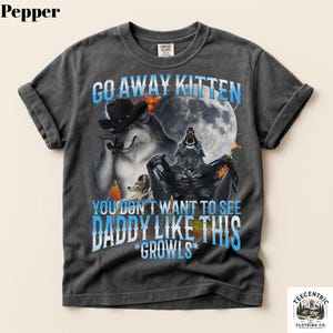 May include: A charcoal gray short-sleeve t-shirt featuring a graphic of two wolves, a full moon, and flames. The text reads: GO AWAY KITTEN YOU DON'T WANT TO SEE DADDY LIKE THIS *GROWLS*. The shirt has a crew neckline and a vintage-style washed finish.