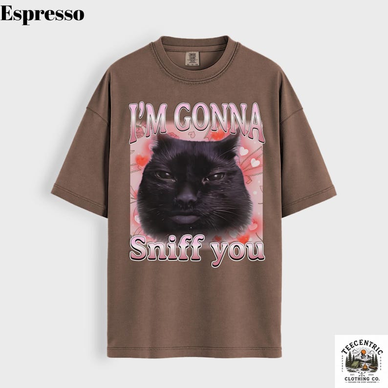 May include: Espresso-coloured t-shirt with a black cat graphic and the text "I'M GONNA Sniff you" in pink. The design includes pink hearts and a butterfly. The tee has a crew neck and short sleeves.
