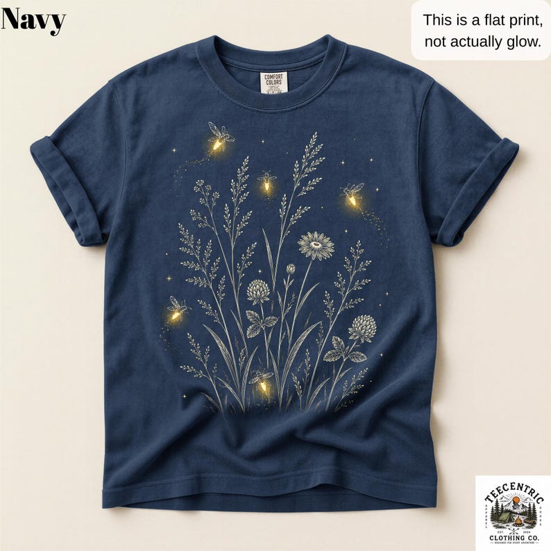 May include: A navy blue t-shirt featuring a white line-art graphic of wildflowers and grasses, accented with yellow firefly illustrations. The text on the shirt reads: Navy, This is a flat print, not actually glow, and TeeCentric Clothing Co.