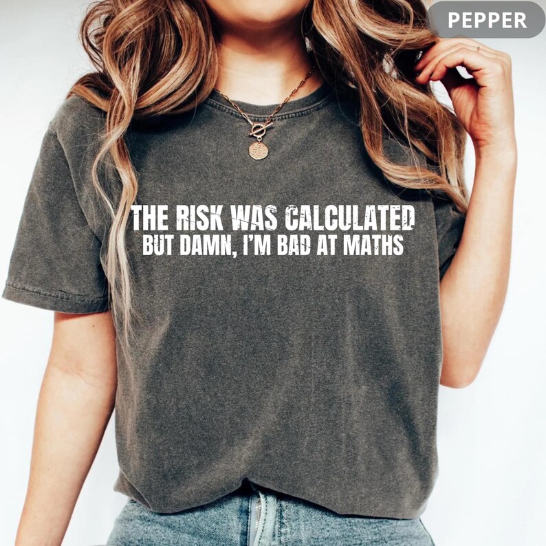 Peut inclure: T-shirt gris fonc&eacute; avec l'inscription blanche "THE RISK WAS CALCULATED BUT DAMN, I'M BAD AT MATHS". Le t-shirt a des manches courtes et un col rond.