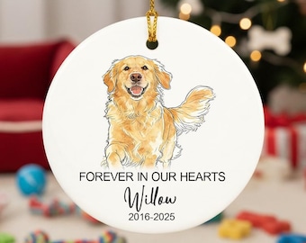 May include: A round, white ceramic ornament with a golden retriever illustration. The text "FOREVER IN OUR HEARTS" is above the name "Willow" and the years "2016-2025". A gold string is attached for hanging. The background includes a Christmas tree.