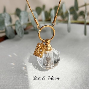 May include: A gold-toned necklace featuring a faceted clear glass orb pendant attached to a circular ring. A rectangular gold charm with a moon and star motif and small clear stones hangs from the ring. The text Star & Moon is printed below.