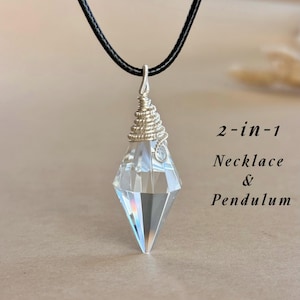 May include: A clear crystal pendant necklace with a silver wire-wrapped top and a black cord. The pendant is a faceted, diamond-shaped crystal. Text on the right reads "2-in-1 Necklace & Pendulum".
