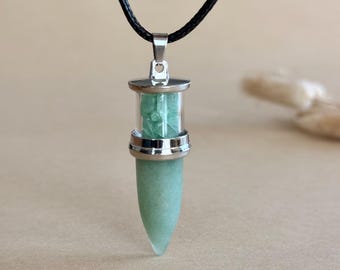 May include: A pendant necklace featuring a bullet-shaped light green stone encased in a silver-toned metal frame with a clear glass cylindrical section containing small green stone chips, suspended from a simple black cord.