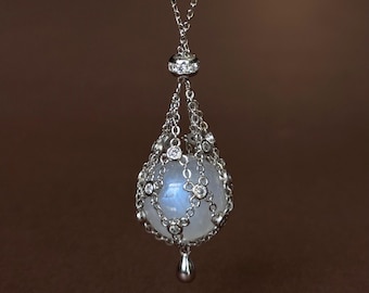 May include: A silver-toned pendant necklace featuring a spherical, translucent white gemstone encased in a delicate, cage-like metal lattice adorned with small, clear, round-cut stones. A small, smooth, teardrop-shaped metal charm hangs at the base.