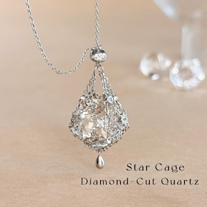 May include: A silver-toned necklace featuring a diamond-cut quartz stone encased in a metal cage adorned with small star shapes and embedded clear stones. The pendant hangs from a delicate chain, with the text Star Cage Diamond-Cut Quartz.