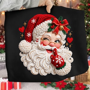 Peut inclure: Un sweat-shirt noir orné d'un motif de Père Noël à l'aspect texturé et crocheté. Le Père Noël porte un bonnet rouge à flocons blancs, des lunettes dorées et un gant rouge avec un flocon blanc, un doigt posé sur les lèvres en signe de silence.