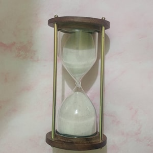 May include: An hourglass with a wooden frame and brass-colored metal supports. The glass bulb contains white sand. The hourglass is a classic timekeeping device, often used for decorative purposes.