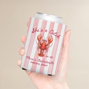 May include: A pink and white striped can cooler with the text "She's a Catch" and a watercolor illustration of a lobster. The text "Olivia's Bachelorette, Portland, Maine, EST. 2025" is also visible.