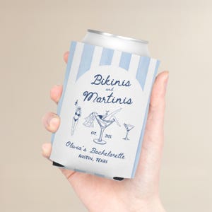 May include: A white and light blue striped can cooler with the text "Bikinis and Martinis" and illustrations of a martini glass and a woman in a bikini. The text "Olivia's Bachelorette, Austin, Texas" is also included.