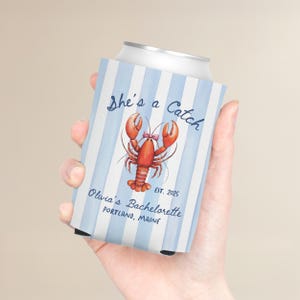 May include: A blue and white striped can cooler with the text "She's a Catch" and a watercolor illustration of a lobster. The text "Olivia's Bachelorette, Portland, Maine, EST. 2025" is also visible.