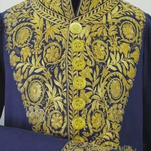 May include: A navy blue jacket with intricate gold embroidery. The jacket features a high collar, gold buttons, and ornate floral and leaf patterns. The sleeve cuffs also have gold embroidery.