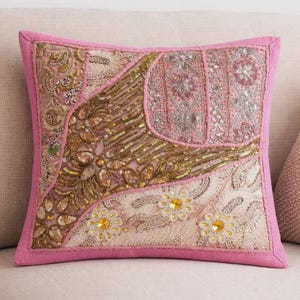 May include: A square throw pillow featuring a pink border and a patchwork design of various fabric panels. The surface is heavily embellished with gold and silver metallic embroidery, intricate beadwork, sequins, and small yellow floral accents.