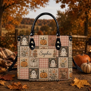 May include: A square handbag featuring a patchwork pattern of ghosts, pumpkins, and floral designs in muted autumn tones. The bag has black handles and a central rectangular label with the name Sophia printed in a dark script font.