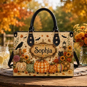 May include: A rectangular handbag with black handles featuring a cream-colored surface decorated with autumn-themed illustrations including pumpkins, sunflowers, a black cat, a crow, bats, and a central plaque with the name Sophia printed in black.