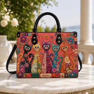 Puede incluir: Un bolso de mano acolchado rectangular con un vibrante estampado floral y cinco gatos estilizados en negro, amarillo, morado, verde azulado y naranja. El bolso tiene asas de cuero negro, una correa de hombro extraíble y el nombre Sophia al frente.